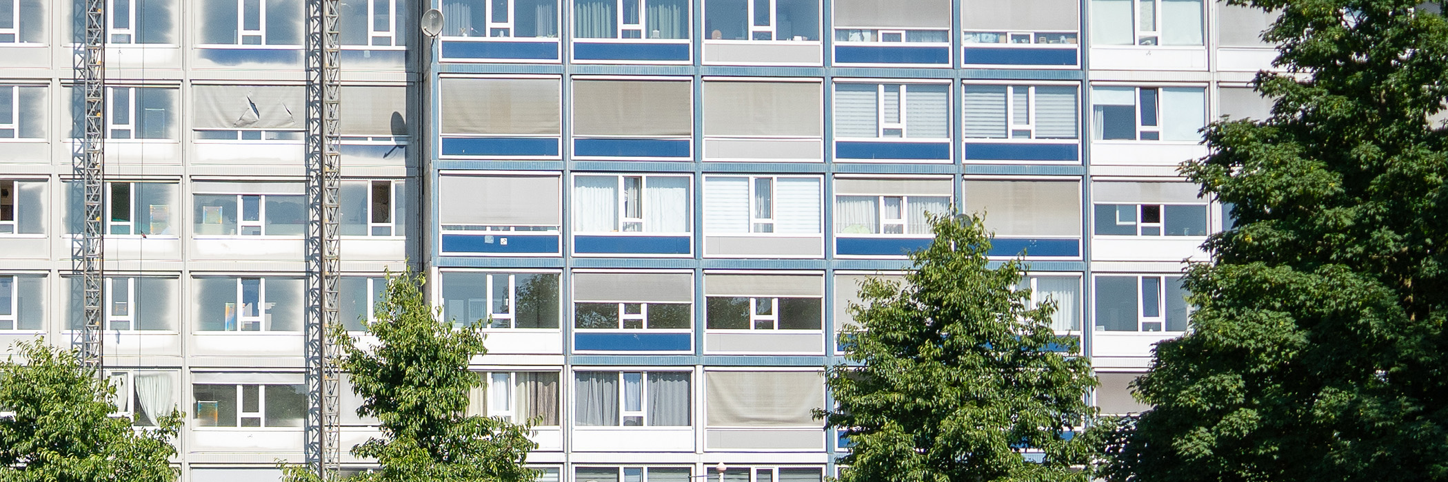 Appartementencomplex met witte kozijnen met blauwe vlakken en bomen ervoor