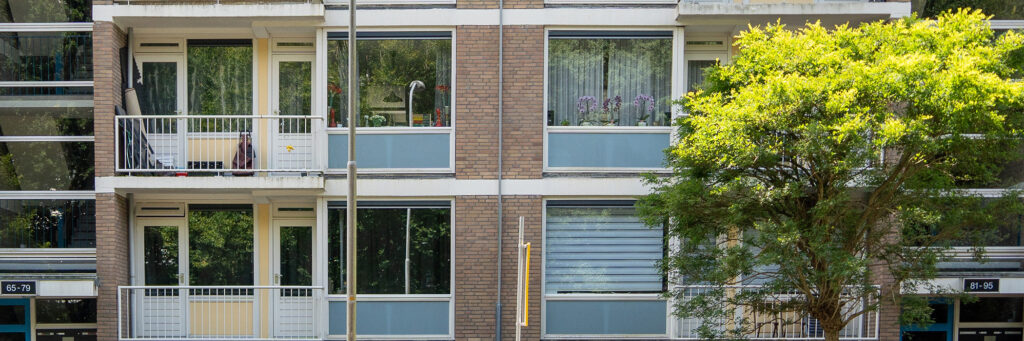 Appartementencomplex met bruine bakstenen gevel, witte kozijnen met blauwe vlakken en witte kozijnen en deuren met een boom ervoor