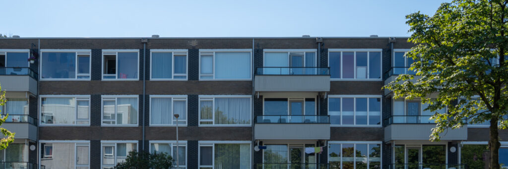 Appartementencomplex met een bruine bakstenen gevel, witte kozijnen, grijze ramen, deuren en balkons en een boom voor de deur