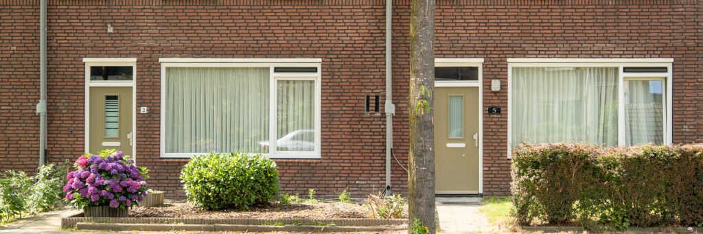Woningen met bruine bakstenen gevel, witte kozijnen, grijze regenpijp en bruingroene deuren