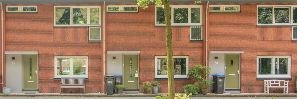Woningen met donker rode bakstenen gevel, witte kozijnen, groene deuren met een boom voor de deur