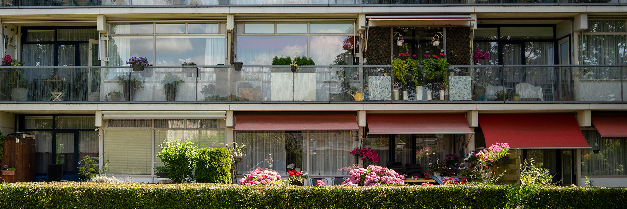 Appartementen met glazen balkons, rode zonwering en een struikje voor de deur
