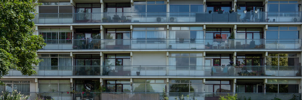 Appartementencomplex met grijze kozijnen, glazen balkons en een boom ervoor