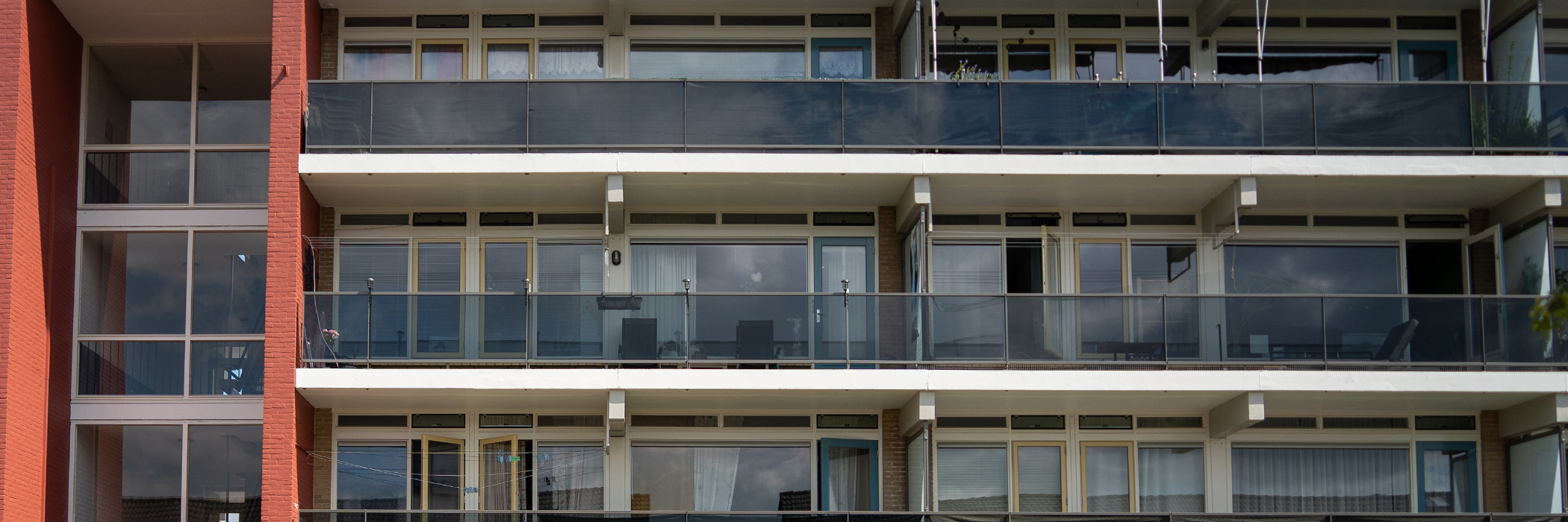 Appartementencomplex met witte kozijnen, gele ramen, blauwe deuren en glazen balkons