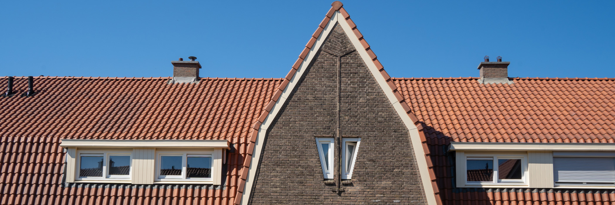 Woningen waarvan de bovenste verdieping is te zien met een punt dak, rode dakpannen en crème gevels