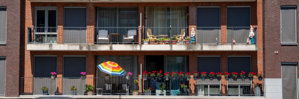 Appartementen met bruine bakstenen gevel, grijze kozijnen en balustrade met planten erop