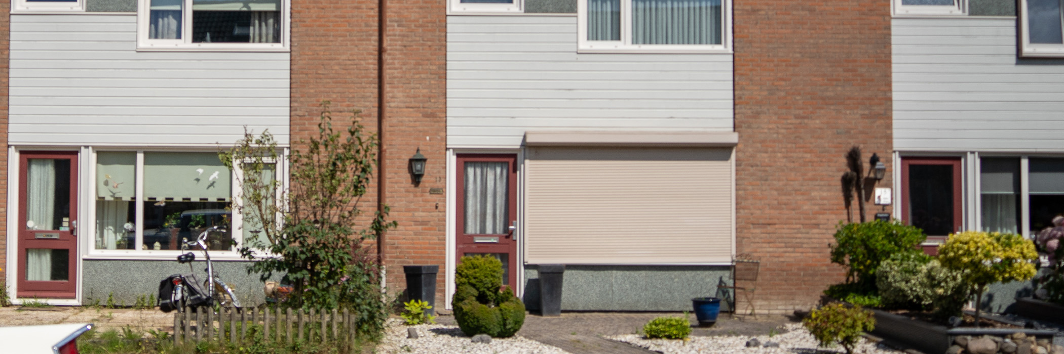 Woningen met bruine bakstenen gevel, witte kozijnen, rode deuren en crème rolluik