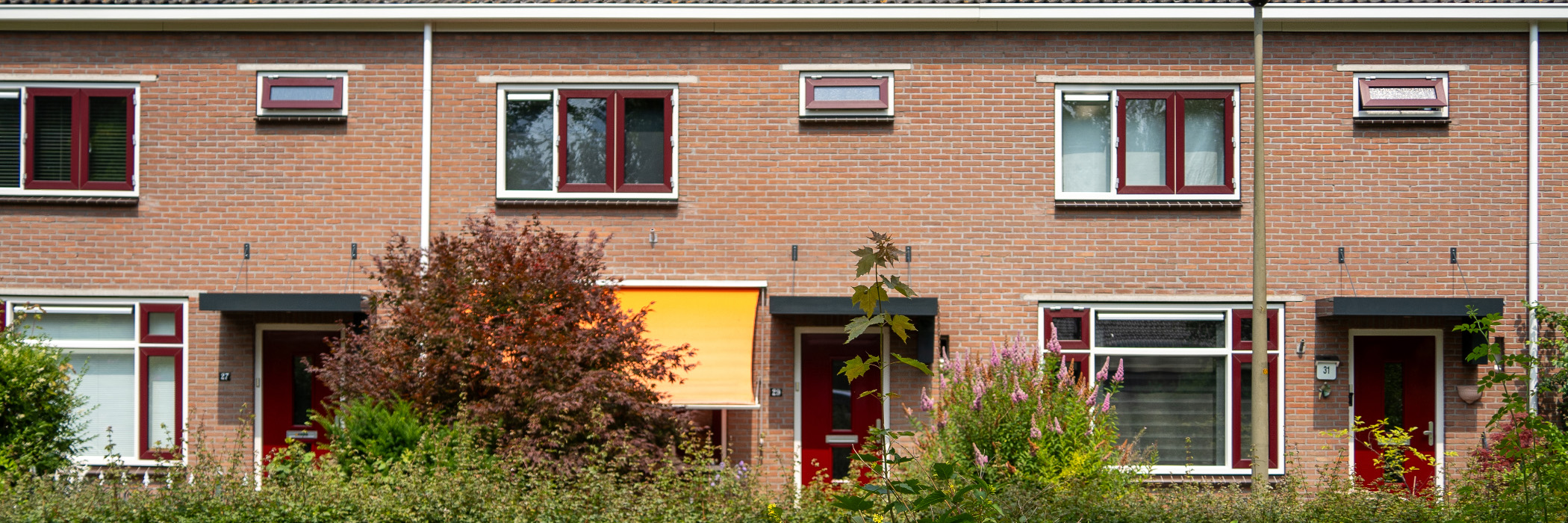 Woningen met bruine bakstenen gevel, witte kozijnen en rode ramen en deuren met veel struiken voor de woningen