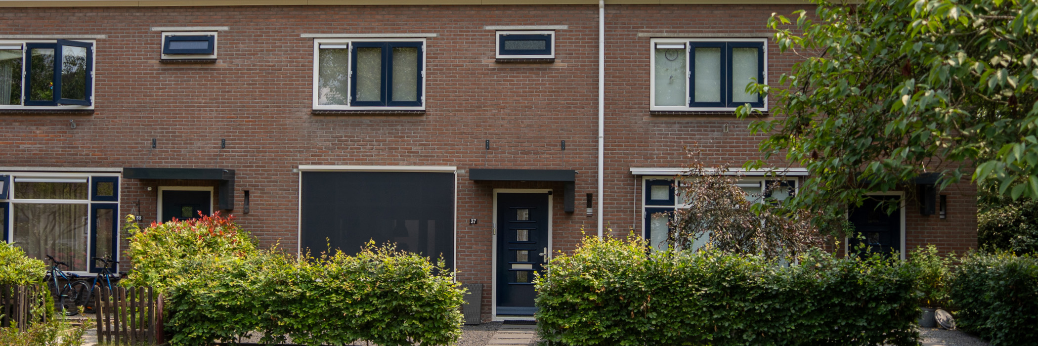 Woningen met bruine bakstenen gevel, witte kozijnen met blauwe ramen en deuren