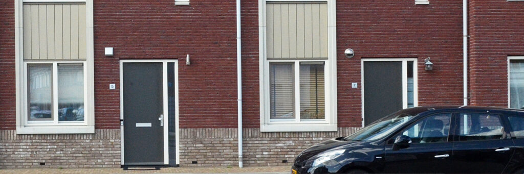 Woningen met donkerrode bakstenen gevel met witte platen, witte kozijnen en blauwe deuren met een zwarte auto