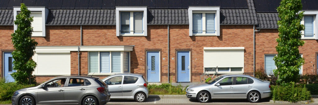 Woningen met bruine bakstenen gevel, witte kozijnen, blauwe deuren en auto's voor de deur met bomen