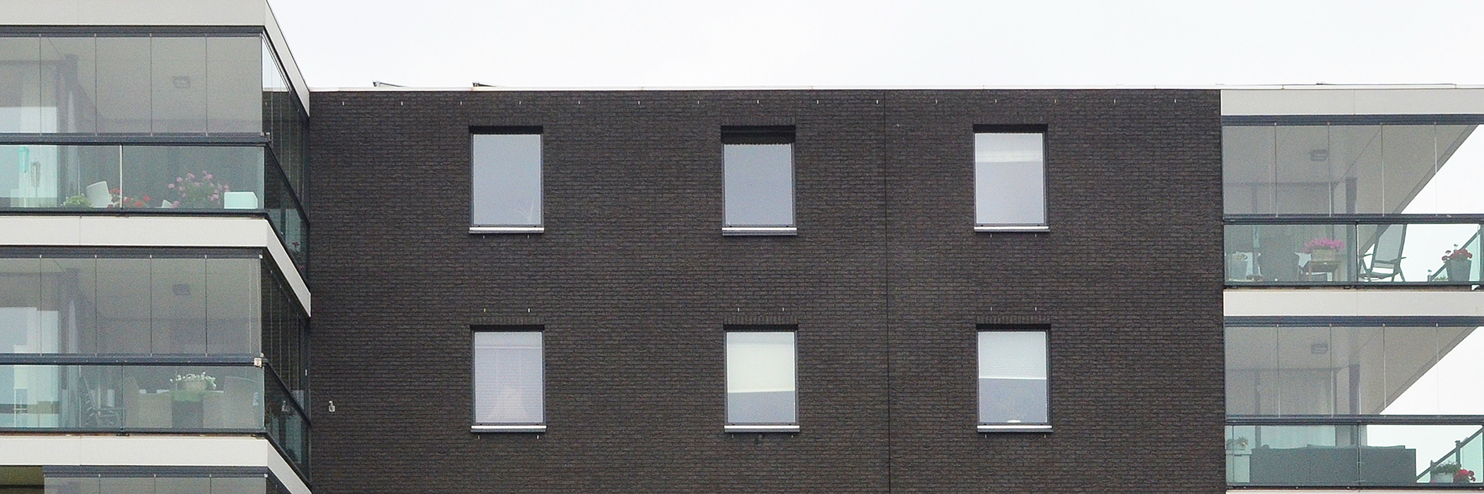 Appartementencomplex met donkerbruine bakstenen gevel met donkere kozijnen en glazen balkons