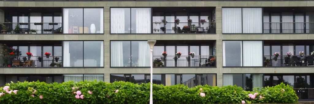 Appartementencomplex met crème bakstenen gevel met donkere kozijnen, lantarenpaal en bomen