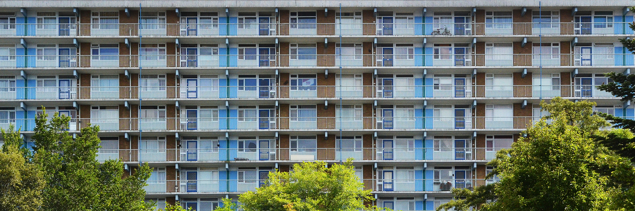 Appartementencomplex met bruine bakstenen gevel, blauwe balustrade en bomen