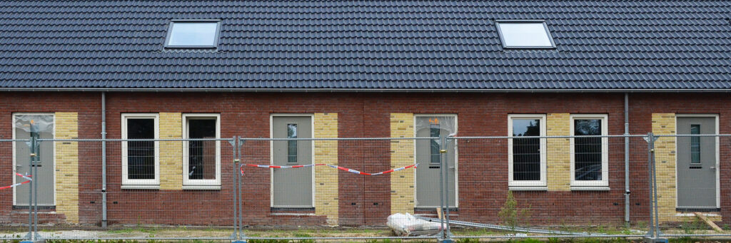 Woning met bruine bakstenen muur, witte kozijnen, grijze deuren met houten platen in de gevel, hek voor de woningen