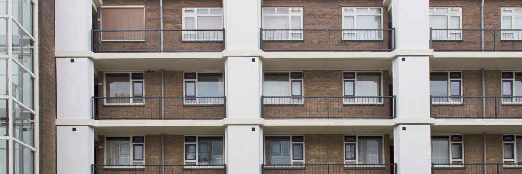 Appartementencomplex met bruine bakstenen gevel met witte stukken, witte kozijnen met grijze ramen en balustrade