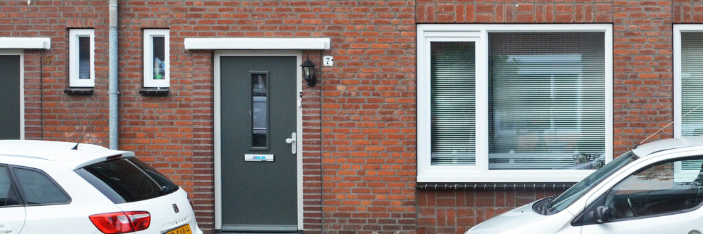 Woningen met donker rode bakstenen gevel, witte kozijnen, grijze deur en twee auto's voor de deur