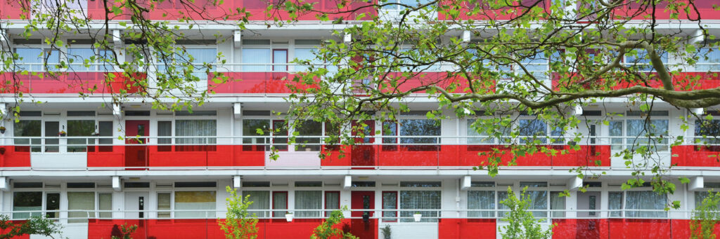 Appartementencomplex met rode deuren en rode balustrade met bomen