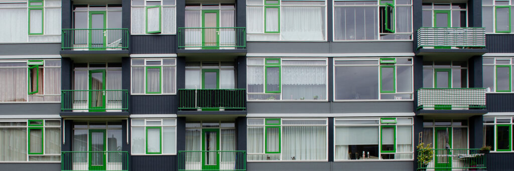 Appartementencomplex met grijze gevel, witte kozijnen en groene ramen, deuren en balustrades