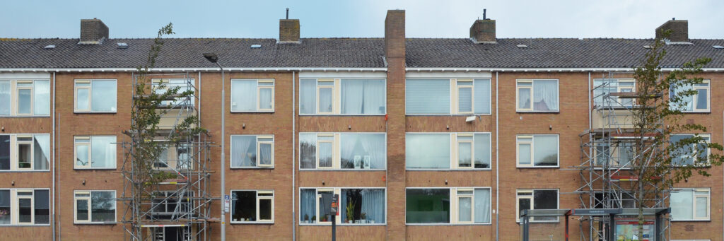 Appartementencomplex met bruine bakstenen muur, donkeren dakpannen, witte kozijnen met gele ramen en steigers voor het complex