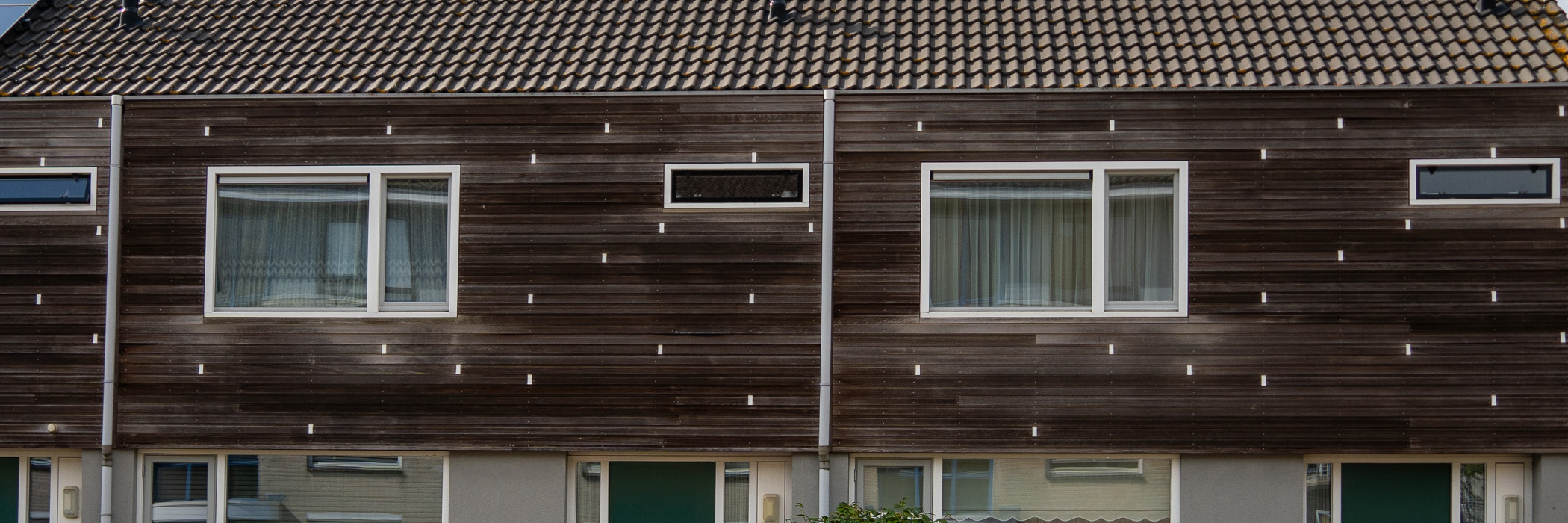 Woningen met bruine houten gevel, witte kozijnen en bruin dakpannen