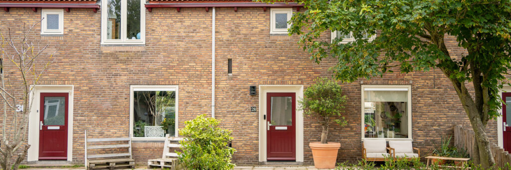 Woningen met bruine bakstenen gevel, witte kozijnen, rode deuren en bomen voor de deur