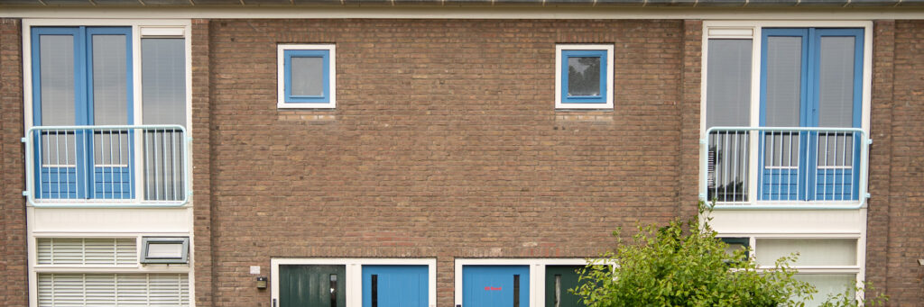 Woningen met bruine bakstenen gevel, witte kozijnen, blauwe ramen en deuren en een boom voor de deur
