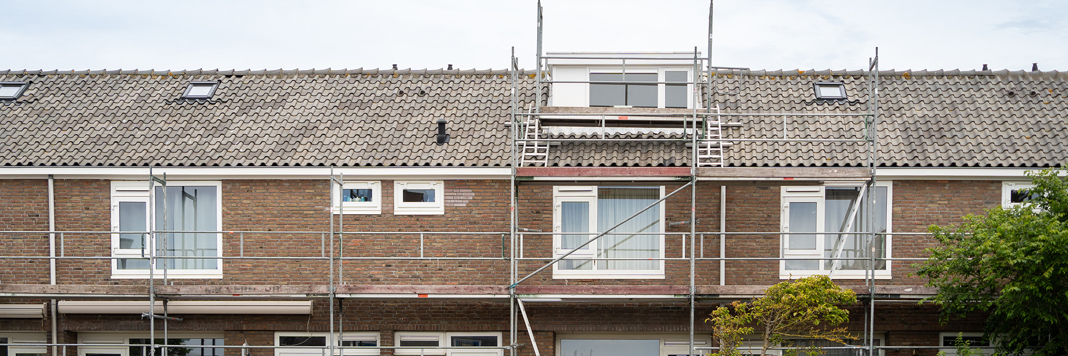 Woningen met bruine bakstenen gevel, grijze dakpannen en witte kozijnen met een steiger voor de deur