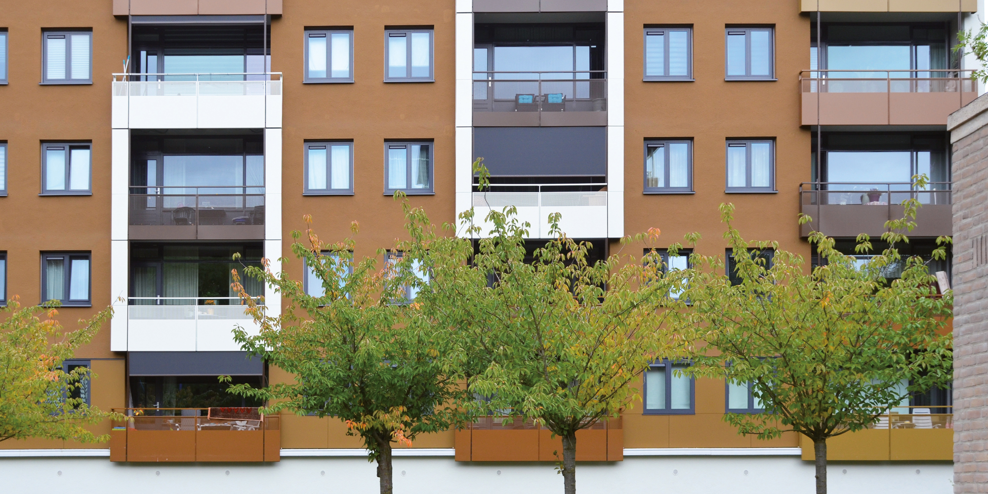 Appartementencomplex met bruine bakstenen gevel met wit en bomen voor de deur