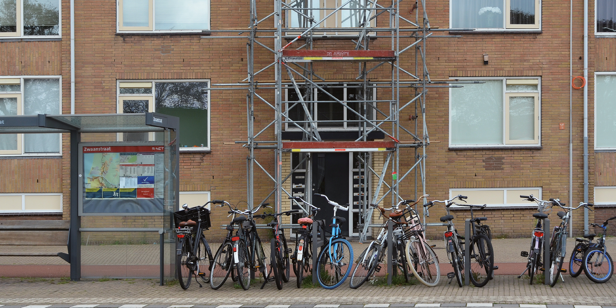 Appartementencomplex met bruine bakstenen gevel, witte kozijnen, steiger voor de deur en fietsen