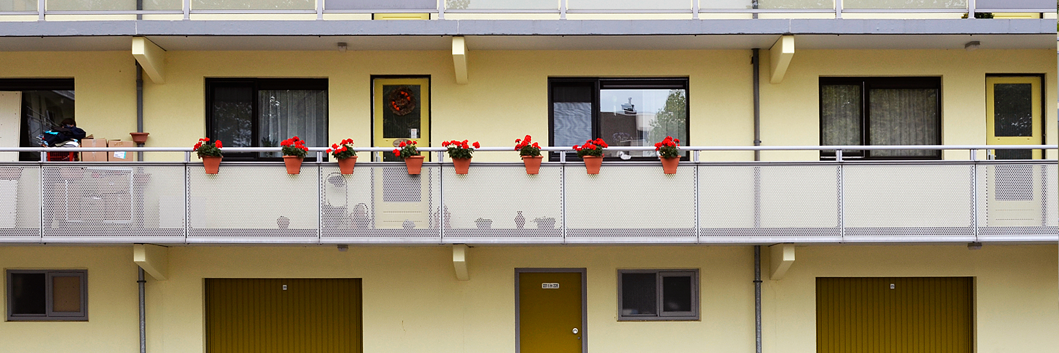 Appartementen met gele gevel, donkerbruine kozijnen, gele deuren en op de begane grond bruine garagedeuren met bloemen aan de balustrade