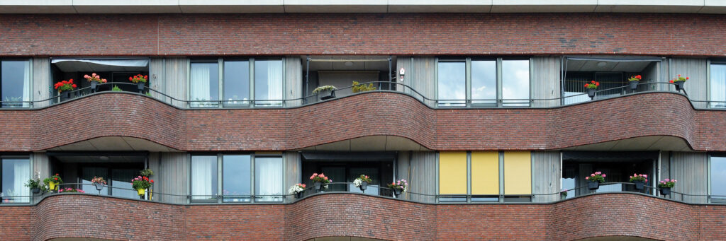 Appartementen met bruin/rode bakstenen gevel, grijze kozijnen met planten aan de balustrade