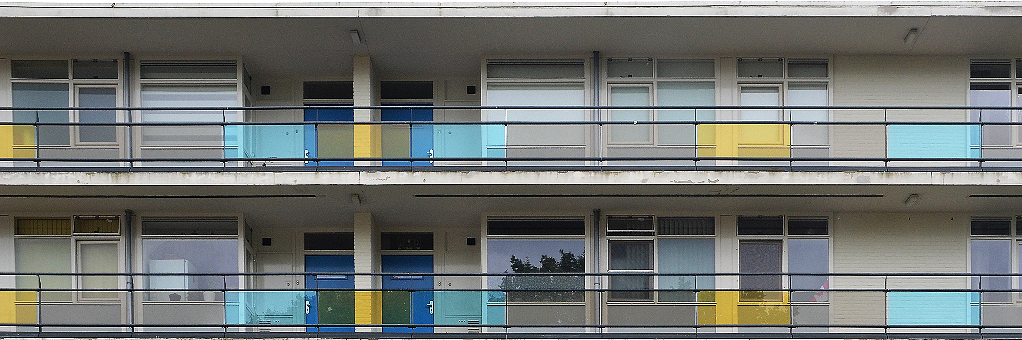 Appartementen met witte bakstenen en kozijnen. De appartementen hebben een balkon met doorzichtig geel en blauw en een donkerdere kleur glas
