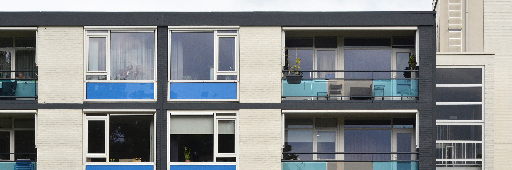 Appartementen met witte bakstenen gevel, witte kozijnen met blauwe platen eronder en blauw grijze balkon balustrades van glas
