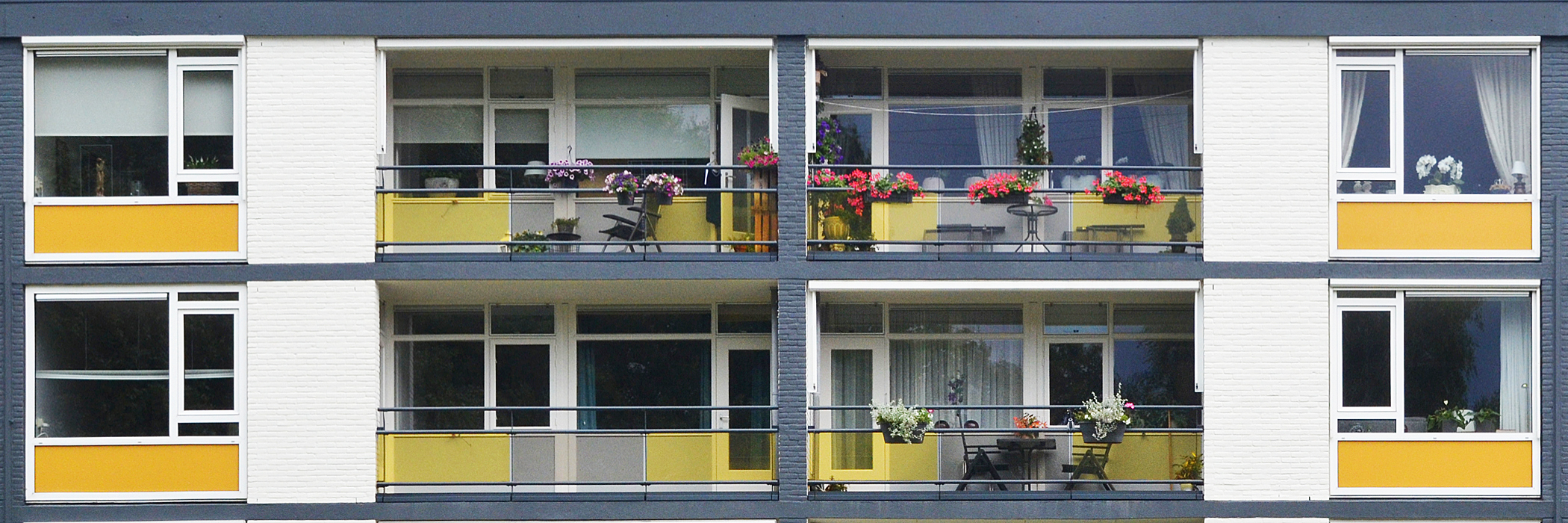 Appartementen met witte bakstenen gevel, witte kozijnen met gele platen eronder, grijze balkon balustrades