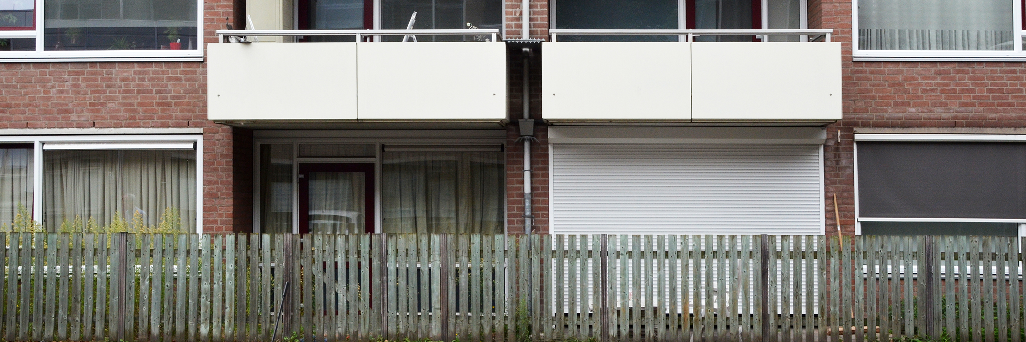Appartementen met bruine bakstenen gevel, witte kozijnen, rode deuren en een hek voor de deur