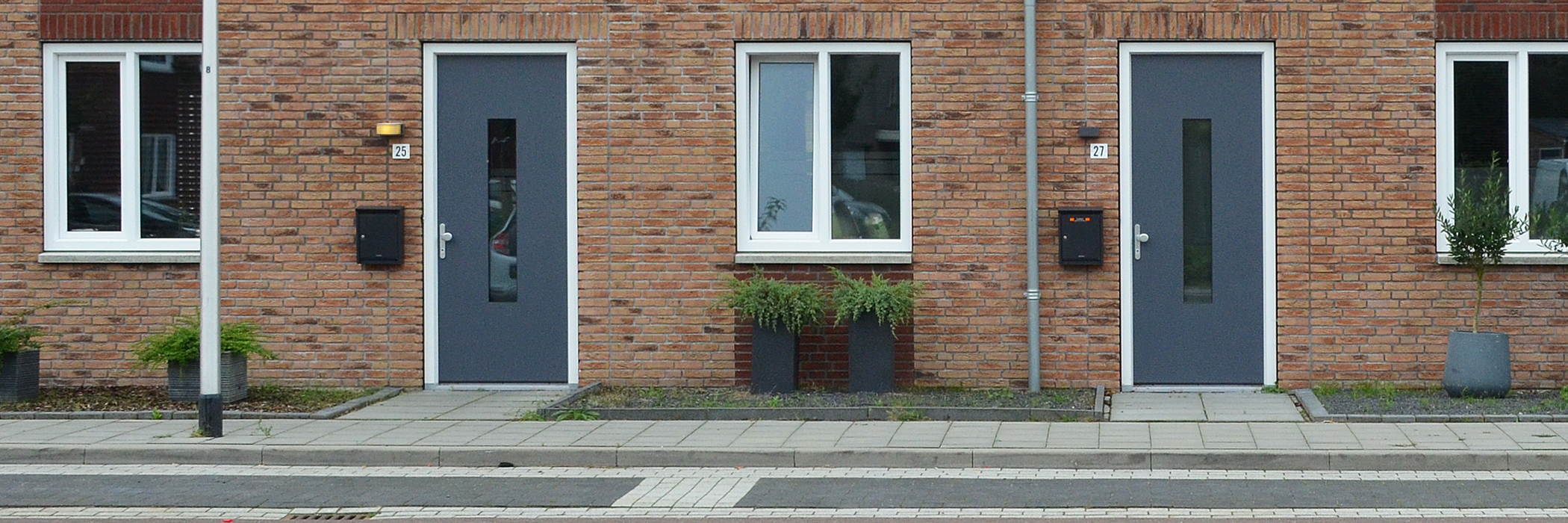 Woningen met bruine bakstenen gevel, witte kozijnen en grijze deuren met daarvoor parkeerplekken