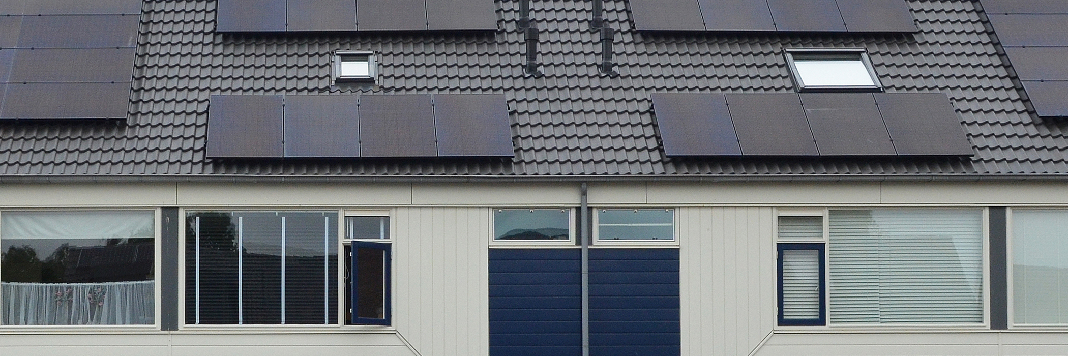 Woningen met witte gevel, zwarte dakpannen met zonnepanelen erop en dakramen met witte kozijnen
