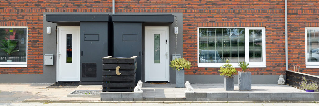 Woningen met bruine bakstenen gevel, witte kozijnen en deuren met de betegelde voortuin