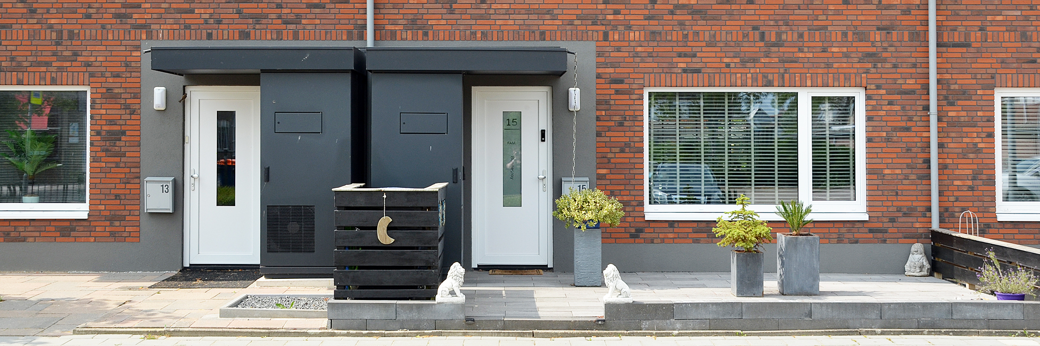 Woningen met bruine bakstenen gevel, witte kozijnen en deuren met de betegelde voortuin