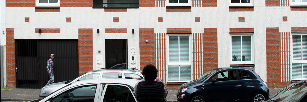 Appartementen met bruin/witte bakstenen gevel, garage en zwarte deur met drie auto's voor de deur waarvan een fiat 500