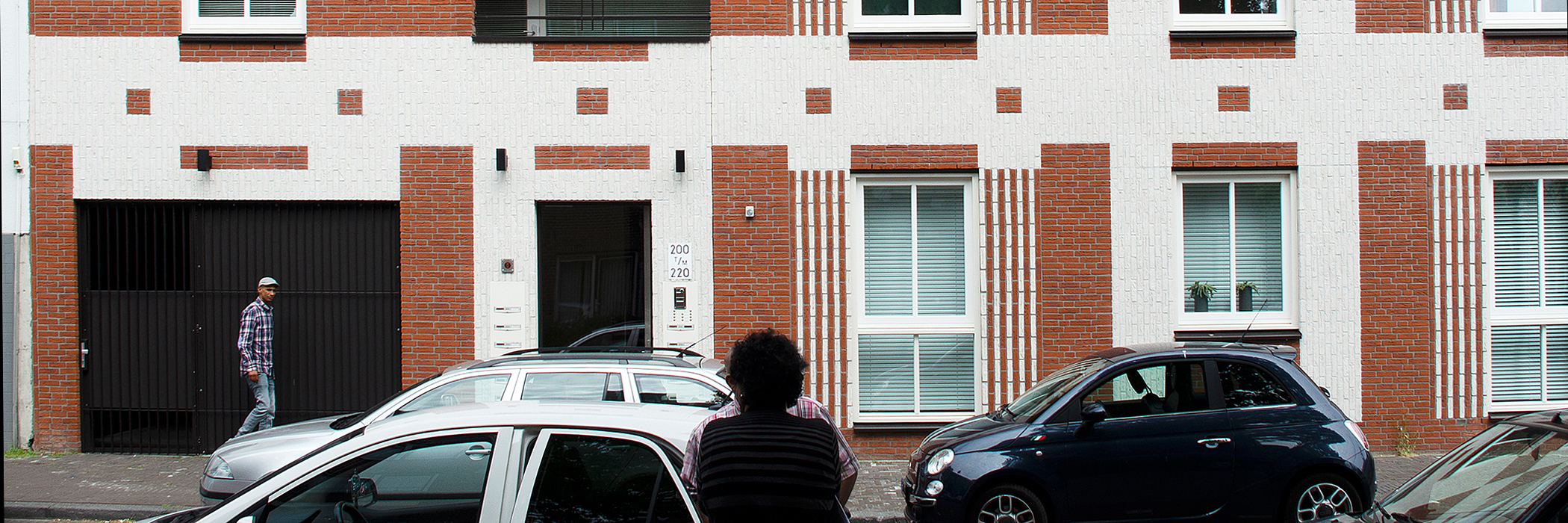 Appartementen met bruin/witte bakstenen gevel, garage en zwarte deur met drie auto's voor de deur waarvan een fiat 500