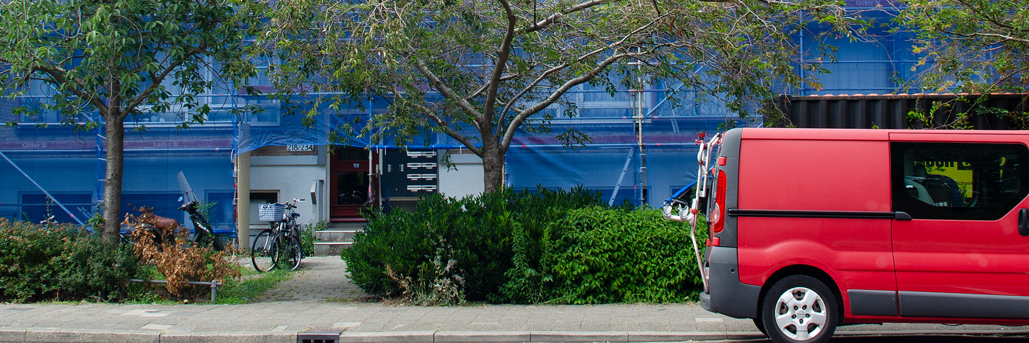 Appartementen in de steigers met blauwe doeken, met bosjes ervoor en een rood busje