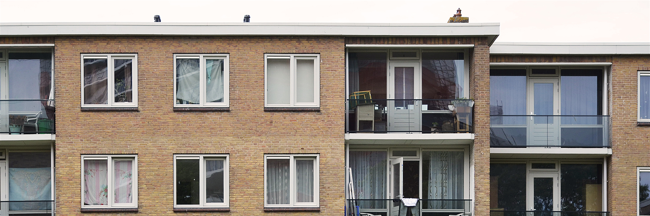 Appartementen met bruine bakstenen gevel, witte kozijnen, zwarte balkons met glas