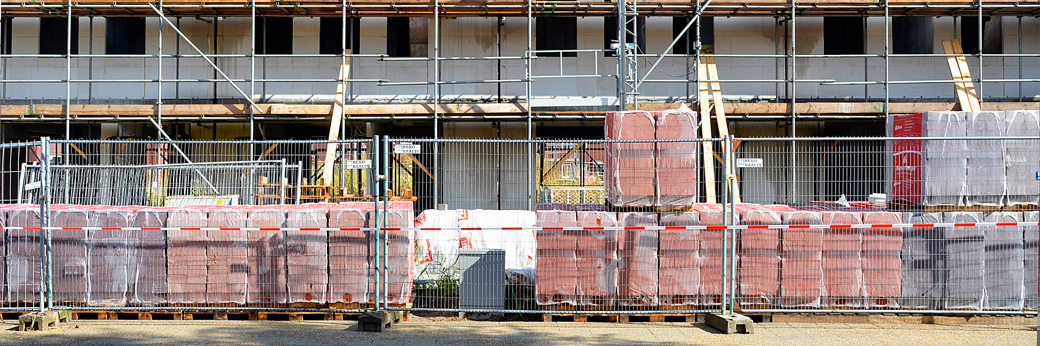 Appartementen in de bouw, met bouwmaterialen die achter een hek staan met een rood wit gestreept lint