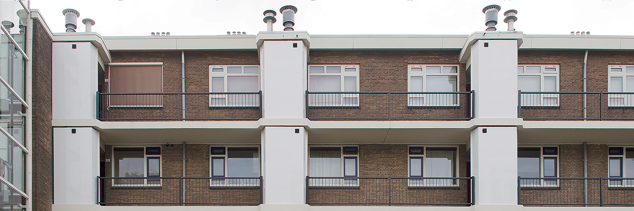 Appartementen met bruine bakstenen gevel. witte kozijnen en grijze balustrades