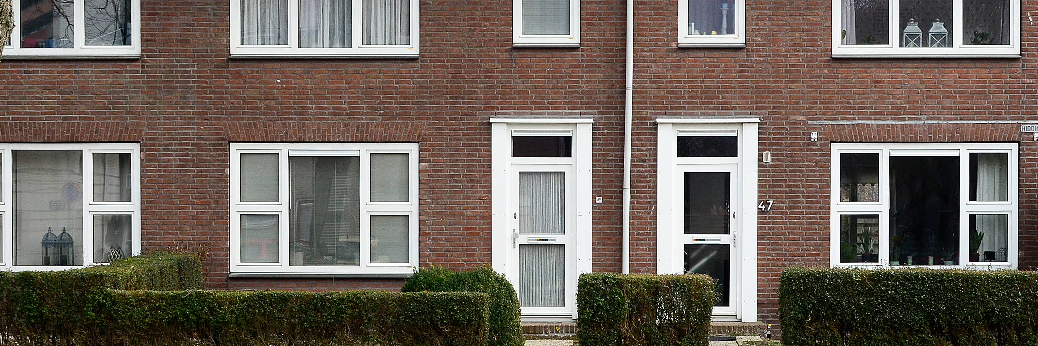 Woningen met rode bakstenen gevel, witte kozijnen en deuren met bosjes voor de deur