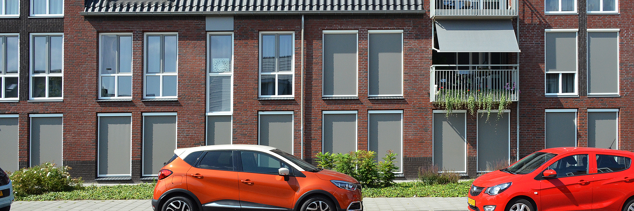 Woningen met rood/bruine bakstenen gevels, witte kozijnen en een oranje en rode auto voor de deur