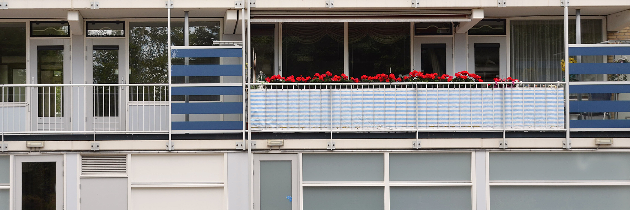 Appartementen met witte balustrades, grijze kozijnen en rode bloemen aan het balkon