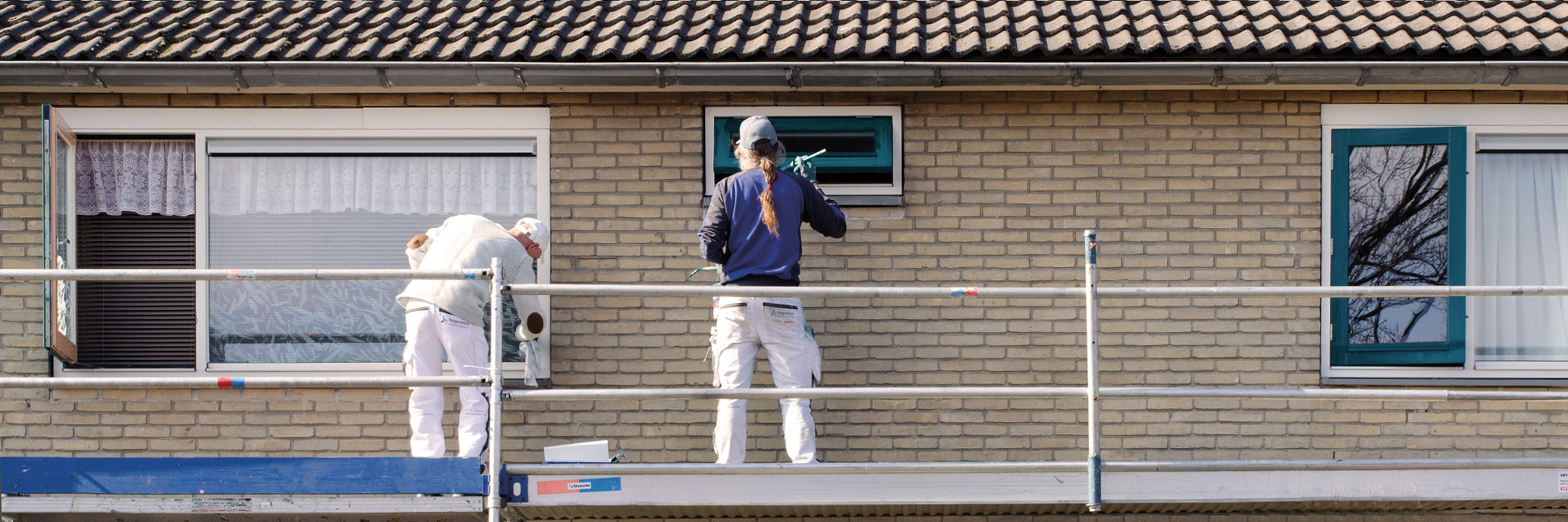 Woningen met crème bakstenen gevel, witte kozijnen waar een steiger voor staat waar twee mannen op staan die aan het werken zijn